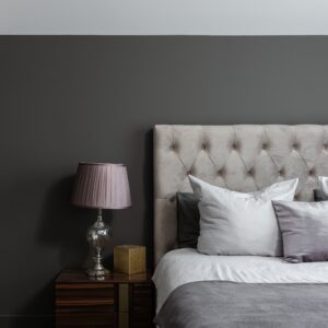 Comfortable bed with soft cushions placed near lamp on bedside table in stylish bedroom with closer and gray wall at home