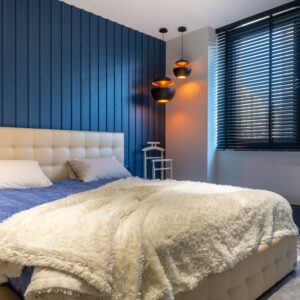Modern bedroom interior with blanket and pillows on bed against lamps and jalousie in house